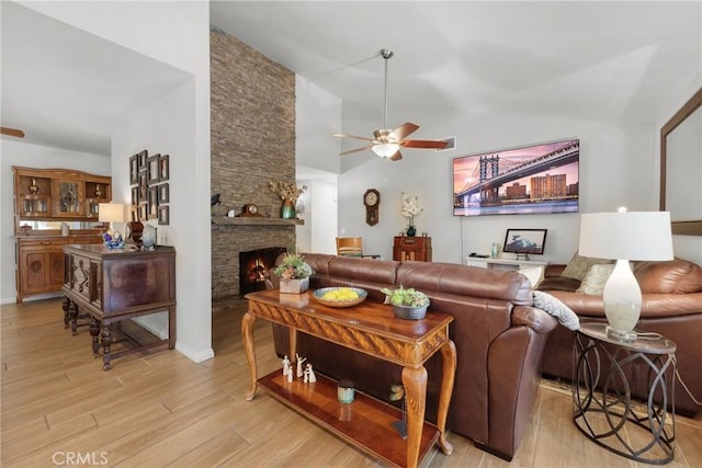 living room featuring ceiling fan, a fireplace, vaulted ceiling, and light wood-type flooring