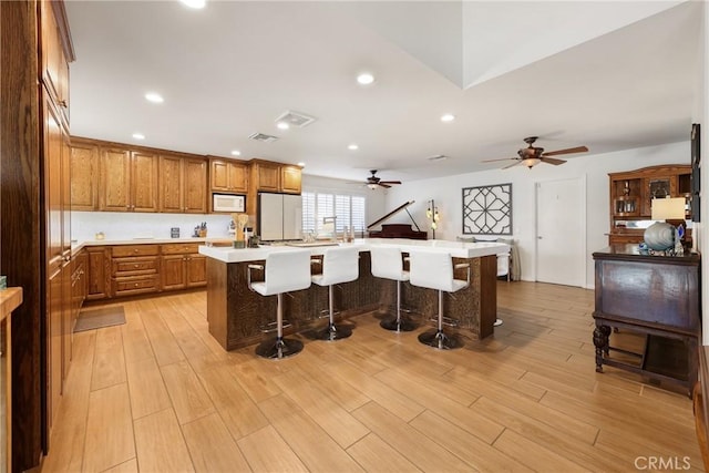 kitchen with ceiling fan, brown cabinetry, a center island, a breakfast bar, and white appliances