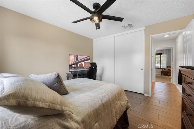 bedroom featuring ceiling fan, light wood-style floors, a textured ceiling, visible vents, and a closet