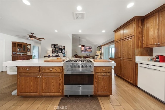 kitchen with high end stainless steel range, dishwasher, brown cabinetry, a ceiling fan, and visible vents