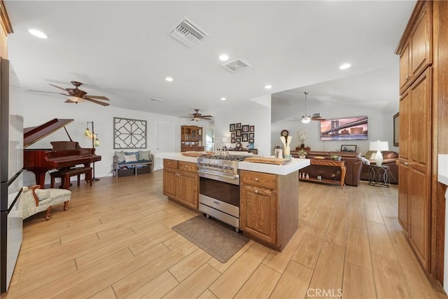 kitchen featuring brown cabinetry, a ceiling fan, light wood-type flooring, light countertops, and open floor plan