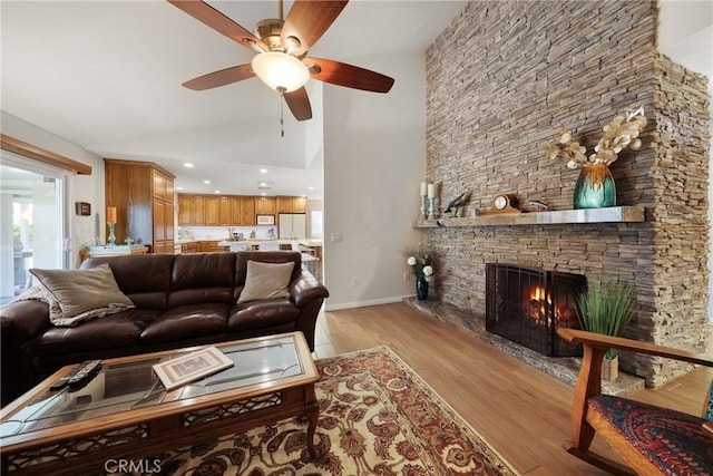 living room with ceiling fan, a fireplace, baseboards, high vaulted ceiling, and light wood finished floors