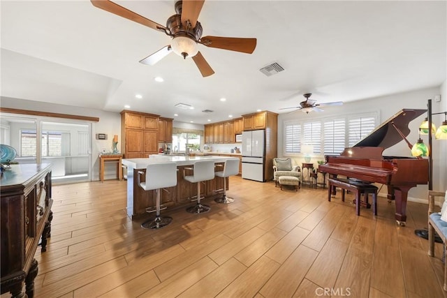 kitchen featuring a breakfast bar, white appliances, light countertops, a ceiling fan, and visible vents