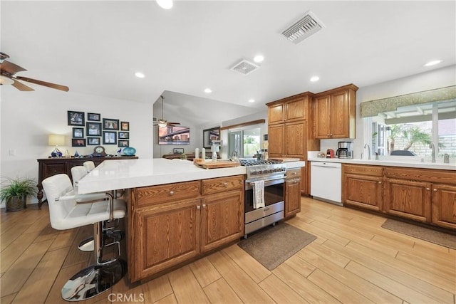 kitchen featuring brown cabinetry, a ceiling fan, visible vents, white dishwasher, and stainless steel stove