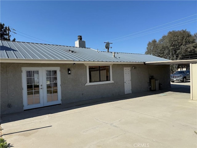 rear view of property featuring stucco siding, french doors, a chimney, and metal roof
