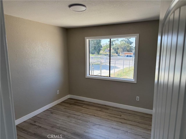 unfurnished room featuring a textured ceiling, baseboards, and wood finished floors