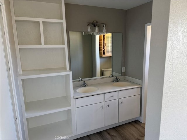 bathroom featuring double vanity, a sink, wood finished floors, and toilet