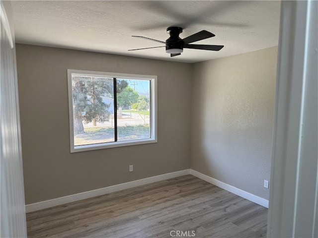 spare room featuring a ceiling fan, baseboards, wood finished floors, and a textured ceiling