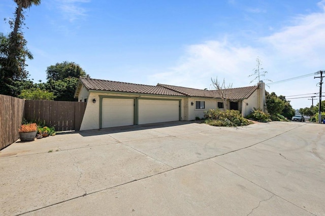 view of front of property with stucco siding, an attached garage, a tile roof, and fence