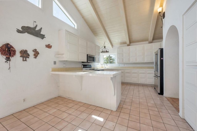kitchen with stainless steel appliances, a peninsula, light countertops, light tile patterned floors, and beamed ceiling
