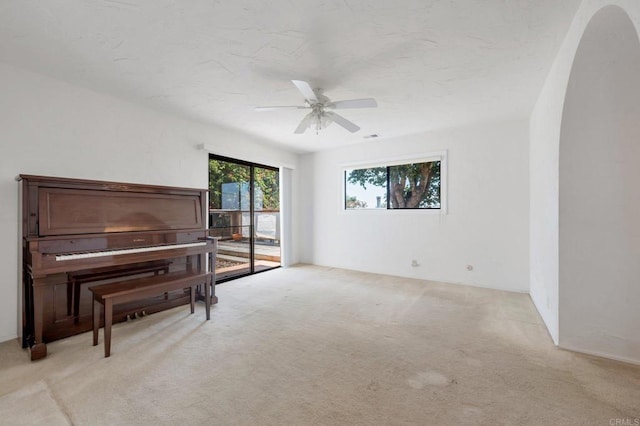 sitting room featuring arched walkways, light carpet, and a ceiling fan