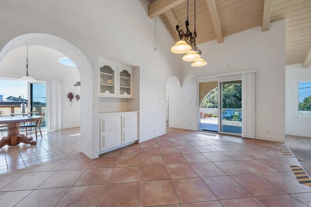unfurnished dining area featuring arched walkways, high vaulted ceiling, light tile patterned floors, beamed ceiling, and wood ceiling