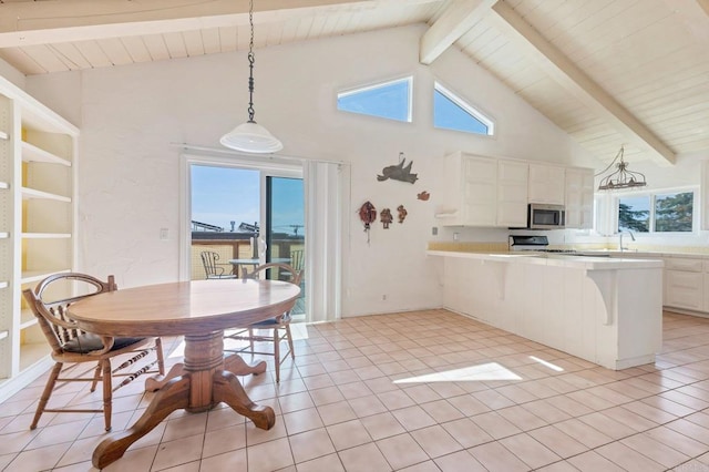 kitchen featuring stainless steel microwave, high vaulted ceiling, beam ceiling, light countertops, and healthy amount of natural light