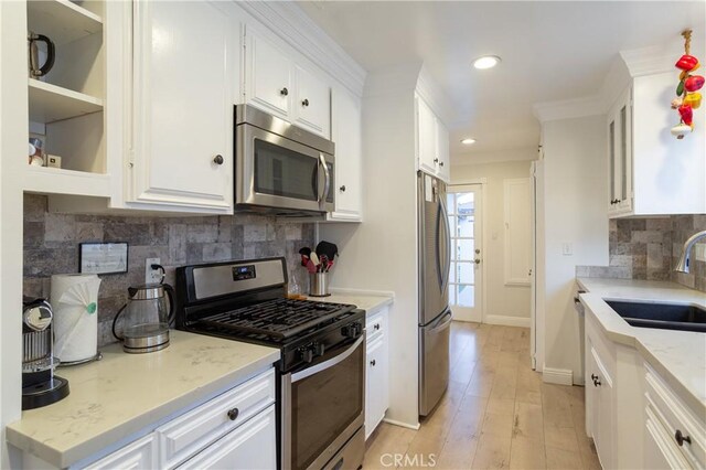 kitchen with stainless steel appliances, light wood-style flooring, a sink, white cabinetry, and decorative backsplash