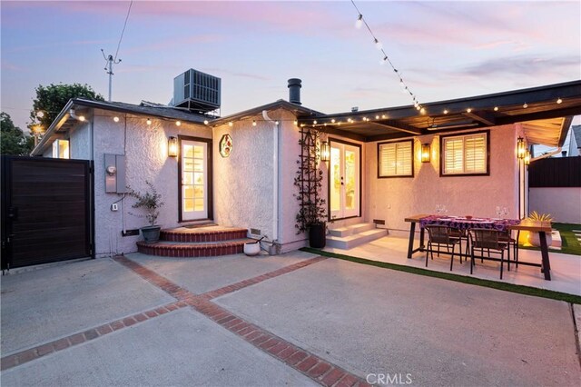 back of property at dusk with a patio area, central air condition unit, driveway, fence, and stucco siding