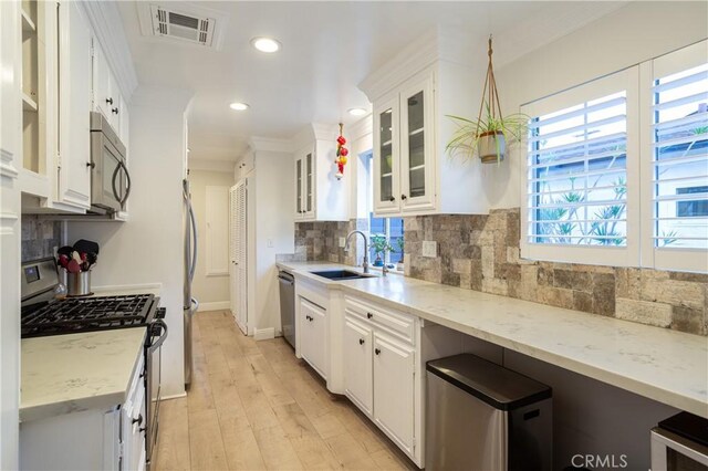 kitchen with tasteful backsplash, a sink, appliances with stainless steel finishes, white cabinetry, and visible vents