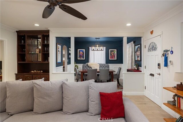 living area with wood finished floors, ceiling fan with notable chandelier, a wainscoted wall, ornamental molding, and recessed lighting