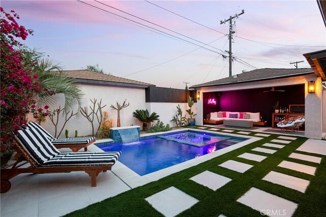 pool at dusk with an outdoor pool, outdoor lounge area, a yard, a patio, and a jacuzzi