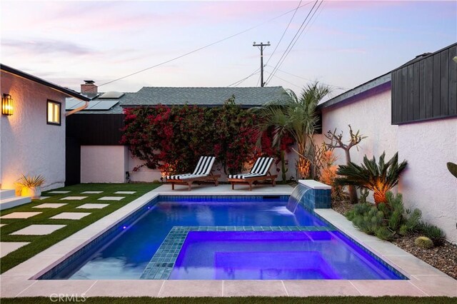 pool at dusk with a lawn and an in ground hot tub