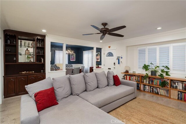 living room with recessed lighting, light wood-type flooring, ornamental molding, and ceiling fan with notable chandelier