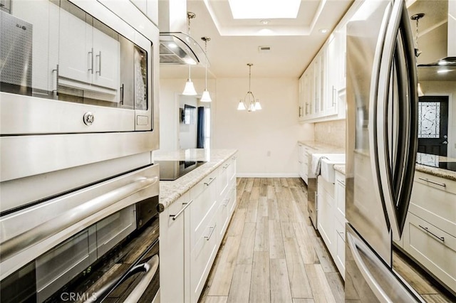 2119 Via Puerta Unit U, Laguna Woods, CA 92637 - kitchen featuring stainless steel appliances, a tray ceiling, light wood-style floors, a skylight, and light stone countertops