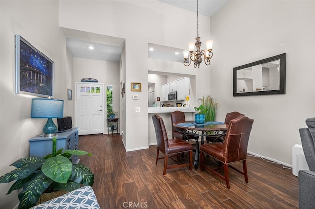 dining space featuring an inviting chandelier, baseboards, dark wood finished floors, and a towering ceiling