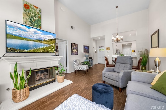 living area with a high ceiling, a notable chandelier, a glass covered fireplace, wood finished floors, and visible vents