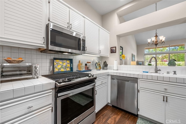 kitchen with tile counters, a sink, dark wood finished floors, backsplash, and stainless steel appliances