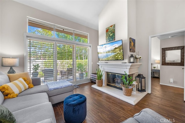 living room with baseboards, a high ceiling, a glass covered fireplace, and wood finished floors