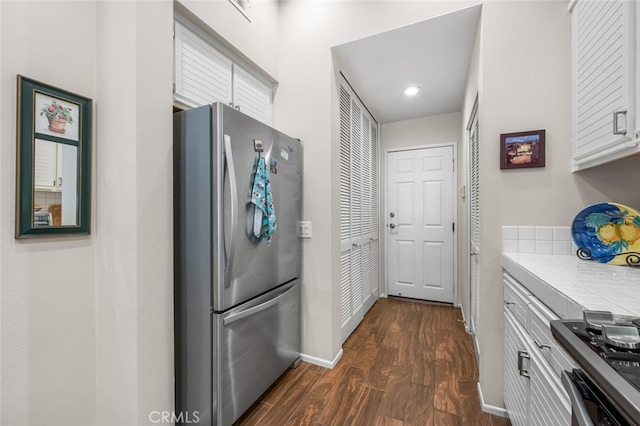 kitchen with appliances with stainless steel finishes, dark wood finished floors, baseboards, tile counters, and white cabinetry