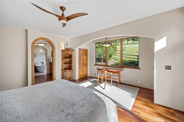 bedroom featuring ceiling fan, arched walkways, light wood-style floors, and ensuite bathroom