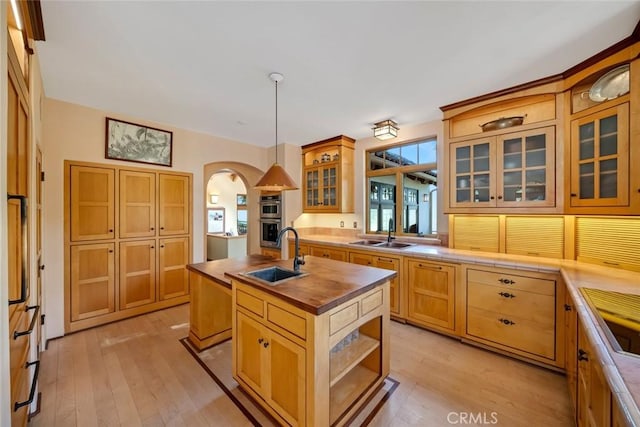 kitchen with light wood finished floors, arched walkways, a sink, and butcher block countertops