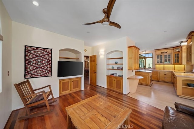 living room with a ceiling fan, built in features, and wood finished floors