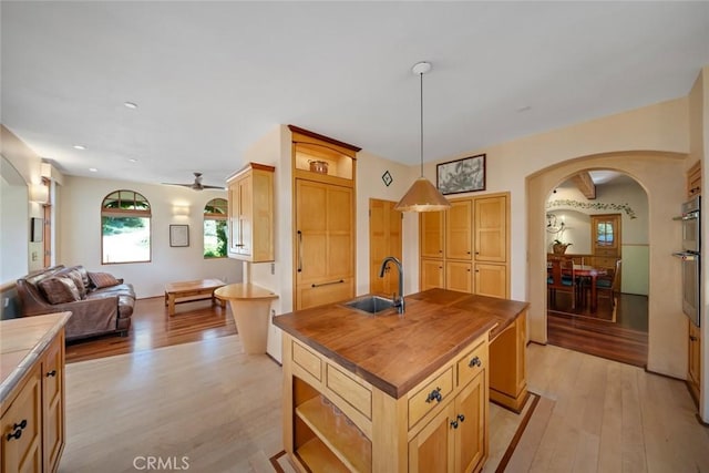 kitchen featuring arched walkways, wood counters, a sink, and light wood-style floors