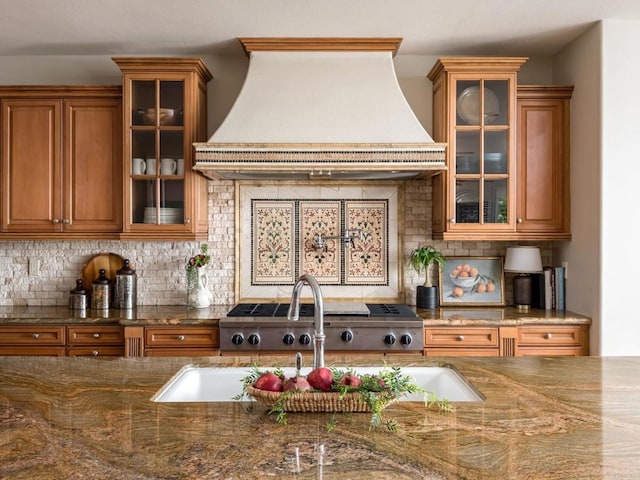 7076 Heron Cir, Carlsbad, CA 92011 - kitchen with premium range hood, brown cabinetry, backsplash, glass insert cabinets, and dark stone countertops
