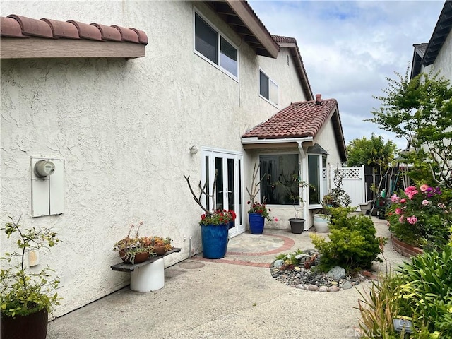 rear view of house with stucco siding, fence, and a tile roof