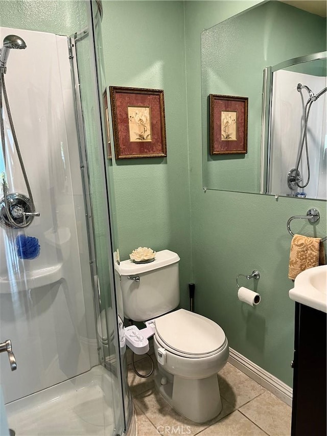 bathroom featuring vanity, toilet, a stall shower, baseboards, and tile patterned flooring
