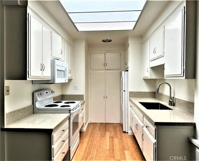 kitchen with light countertops, a sink, white appliances, light wood-type flooring, and white cabinetry