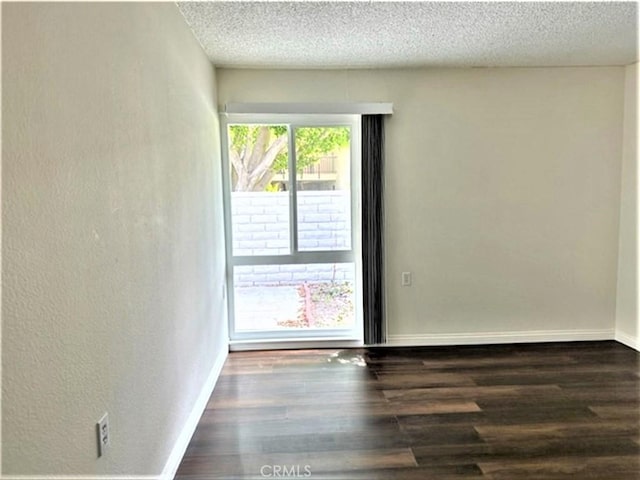 empty room with wood finished floors, a textured ceiling, baseboards, and a textured wall