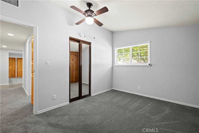 unfurnished bedroom featuring a ceiling fan, a closet, dark carpet, baseboards, and visible vents