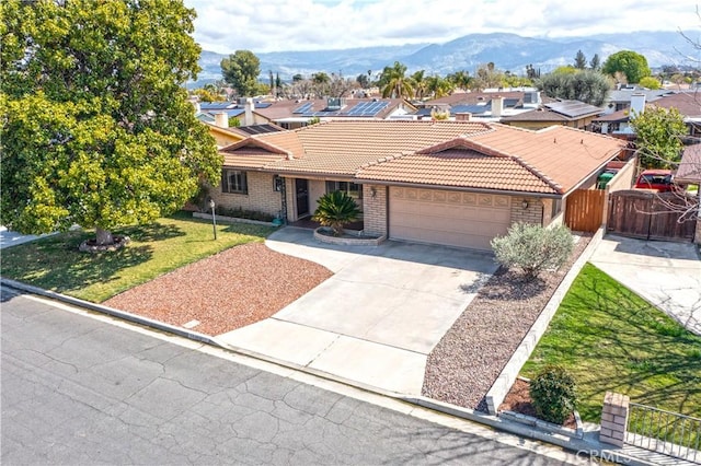 ranch-style house featuring a tile roof, concrete driveway, fence, a garage, and brick siding