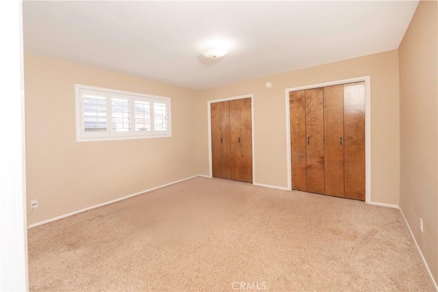 unfurnished bedroom with carpet floors, multiple closets, and baseboards