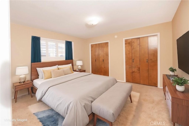bedroom featuring baseboards, two closets, and light colored carpet