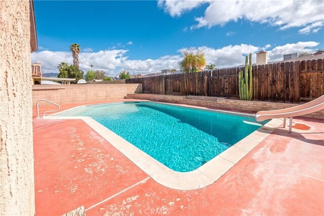 view of pool with a fenced backyard, a water slide, a fenced in pool, and a patio