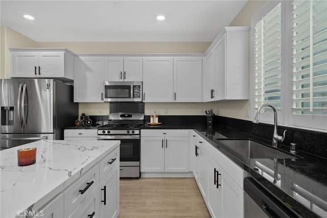 kitchen with light wood finished floors, stainless steel appliances, dark stone countertops, a sink, and white cabinetry