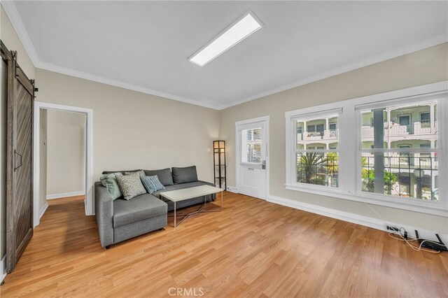 living area with light wood-type flooring, baseboards, crown molding, and a barn door