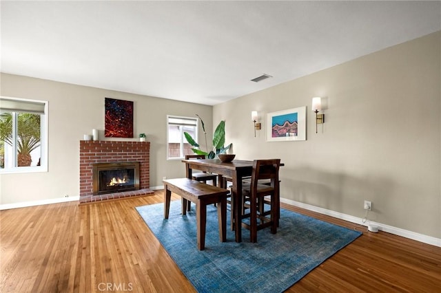 dining area with a brick fireplace, wood finished floors, visible vents, and baseboards