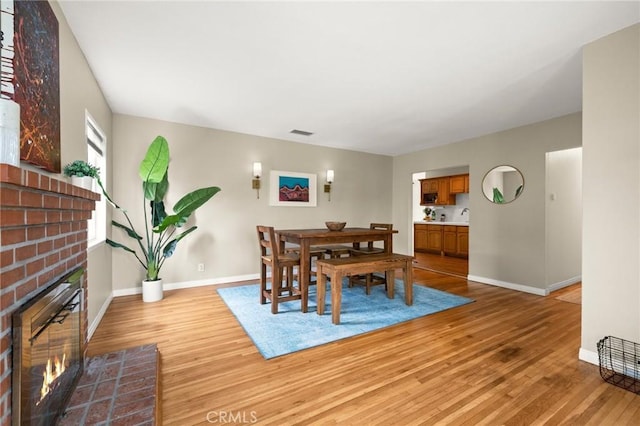 dining room featuring light wood-type flooring, baseboards, a fireplace, and visible vents