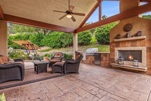 view of patio / terrace featuring an outdoor kitchen, ceiling fan, a lit fireplace, and area for grilling