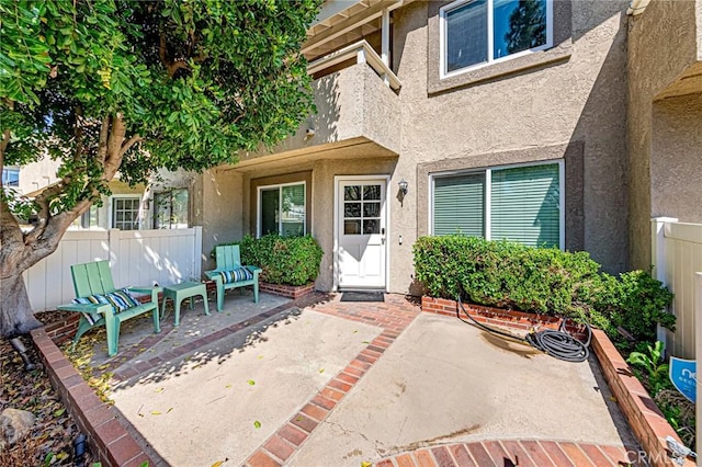 entrance to property with a patio, fence, and stucco siding